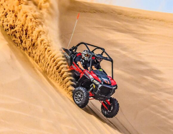 Red Polaris RZR buggy carving down a sand dune