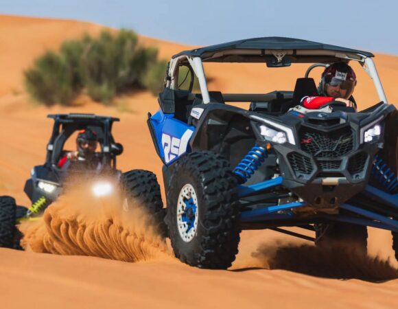 Blue Can-Am Maverick buggy kicking up sand on the Dubai dunes