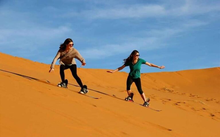 Two guests sandboarding down a dune on the morning desert safari