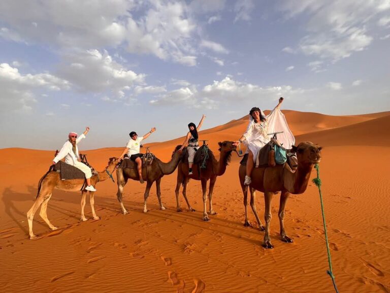 Guests on a camel trek across the red dunes under a blue sky